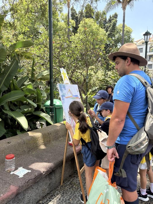 People gathered around an easel in the park, watching a drawing take shape.