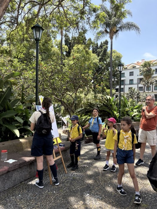 Someone painting at an easel in Parque de Santa Catarina while a group of children in yellow shirts stops to watch.